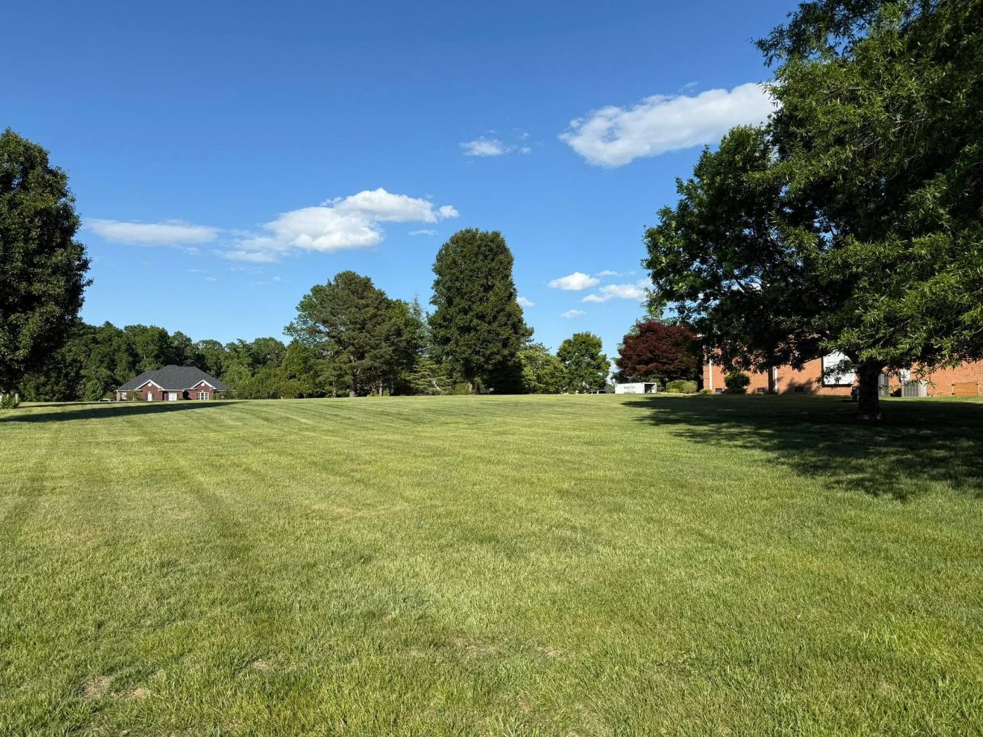 Wide open acreage mowed in even stripes, running between mature trees and a brick building