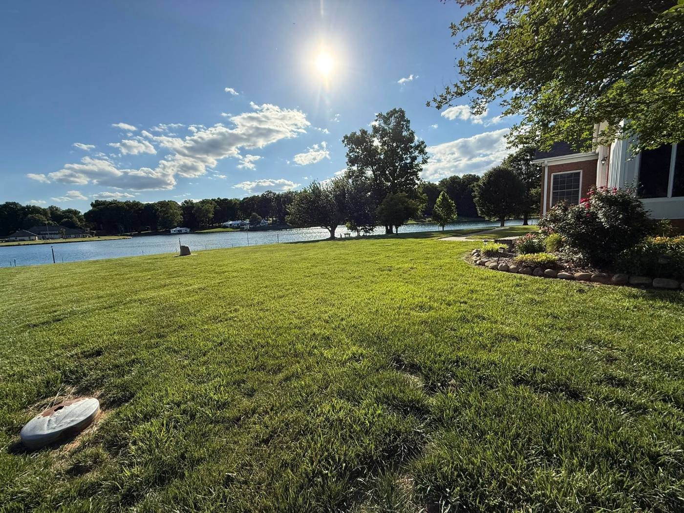 Freshly mown lakefront lawn running down to the water, with stone-bordered flower beds along the brick home